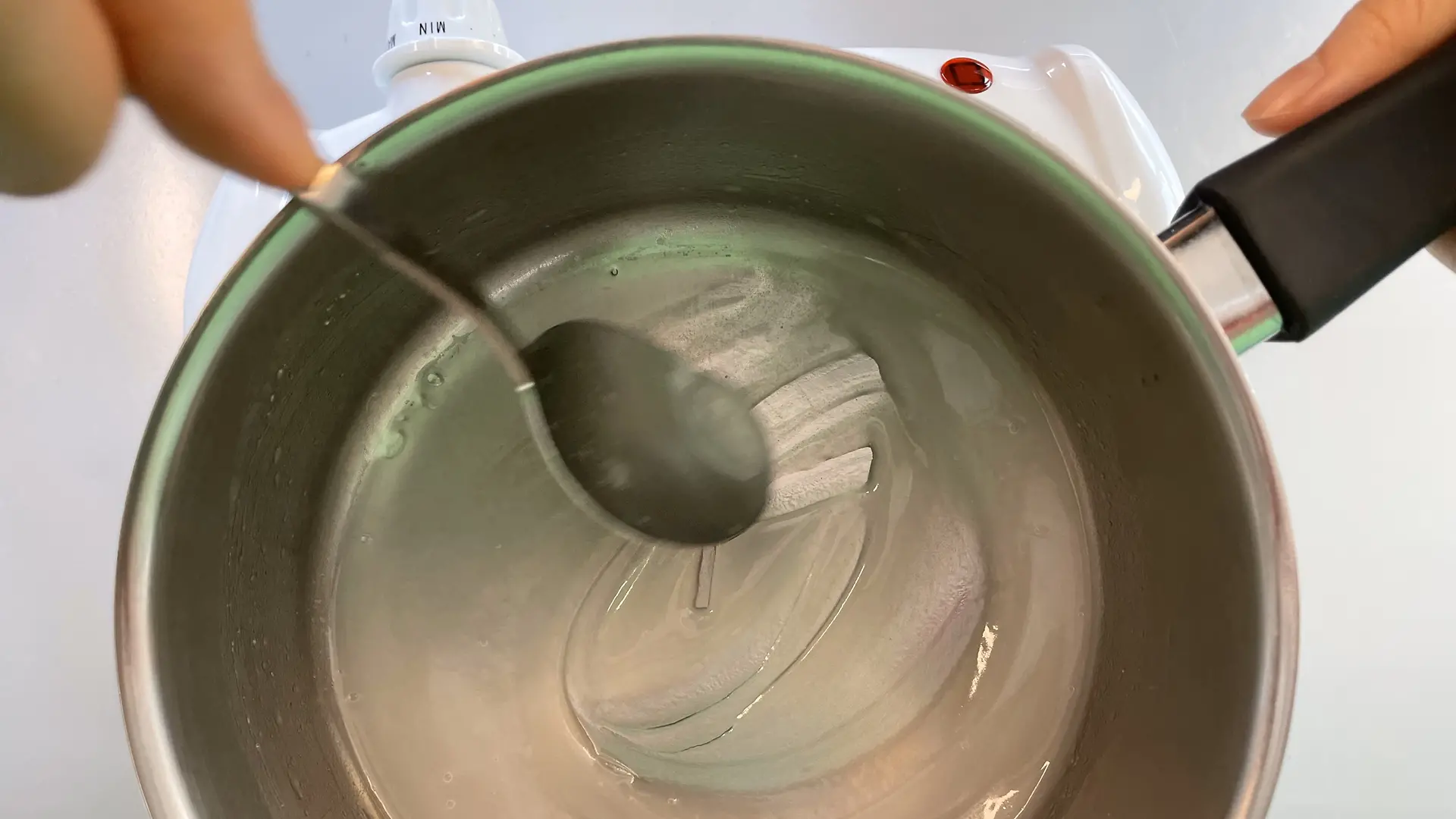 Kleiner Kochtopf mit Stärke-Mischung, die mit einem Löffel verrührt wird.