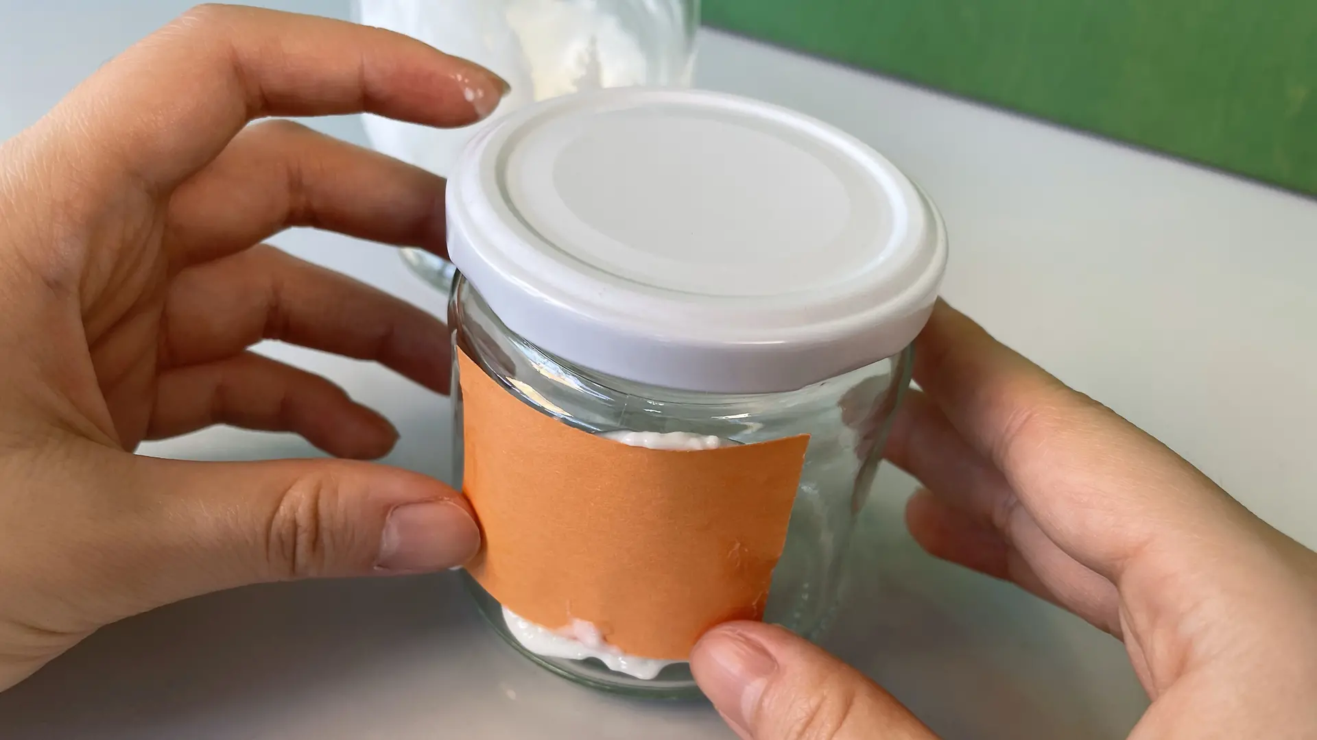 Ein mit Kaseinkleber bestrichenes Papierstück wird an das Marmeladenglas geklebt. 