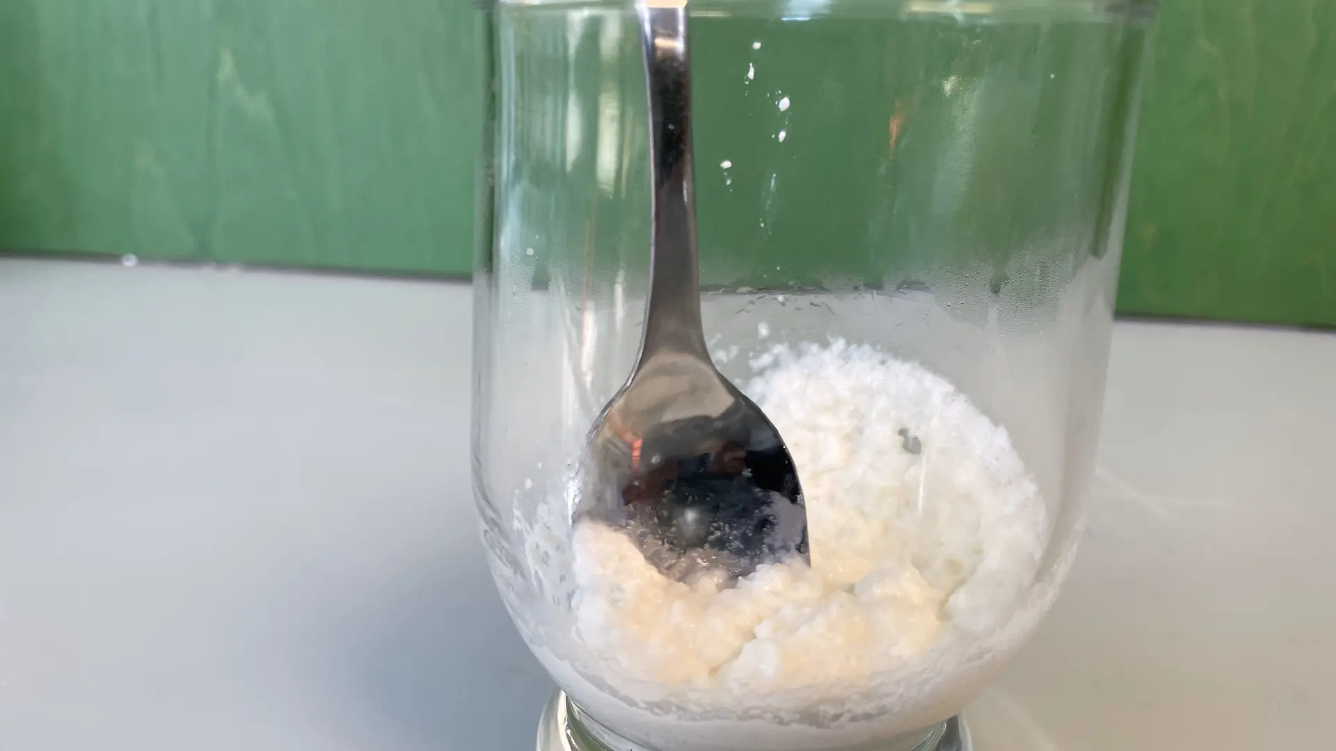 Glas mit Milchproteinen, etwas Wasser und Backpulver. Die Masse wird mit einem Löffel gerührt.