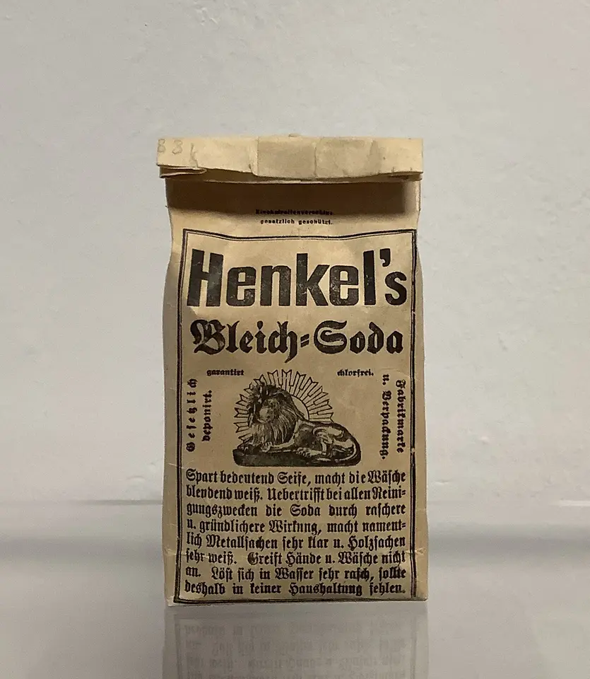 Braune Papierverpackung des Produkts „Henkel’s Bleich-Soda“ mit schwarzer Schrift und einer Illustration eines Löwen. Das Produkt steht auf einer glatten Oberfläche.