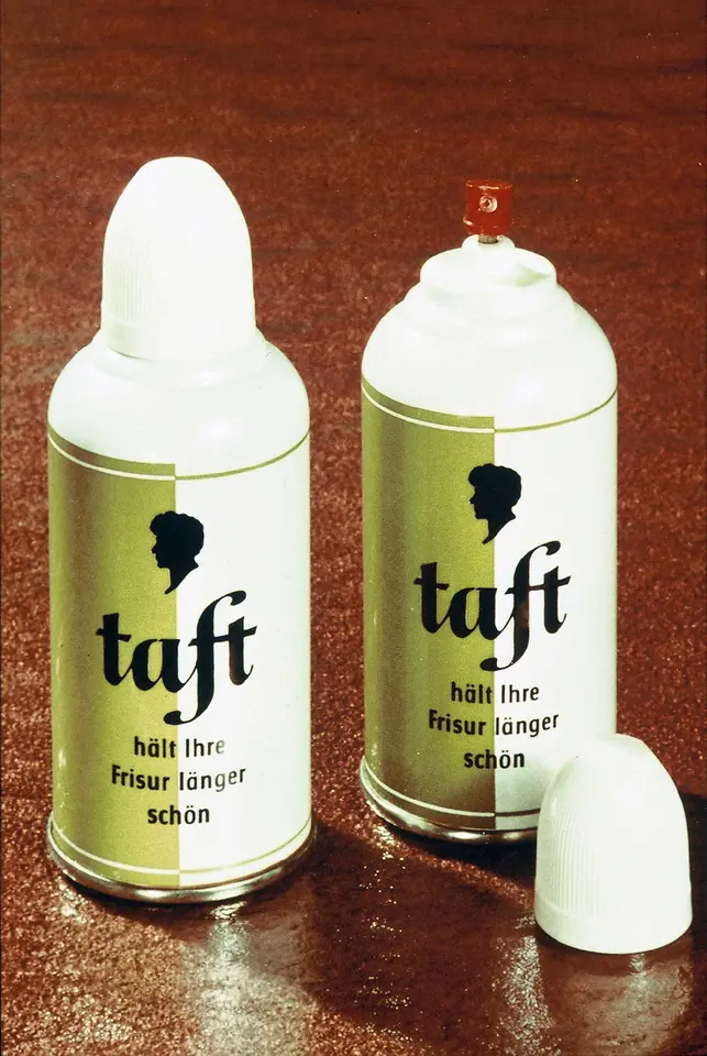 Zwei metallische Spraydosen der Marke Taft mit gold-weißer Gestaltung und schwarzer Schrift. Eine Dose ist geöffnet und zeigt das rote Sprühventil.